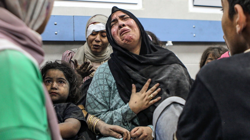 A woman cries as she sits next to a girl covered in dust and in front of an injured woman with an eye bandage.