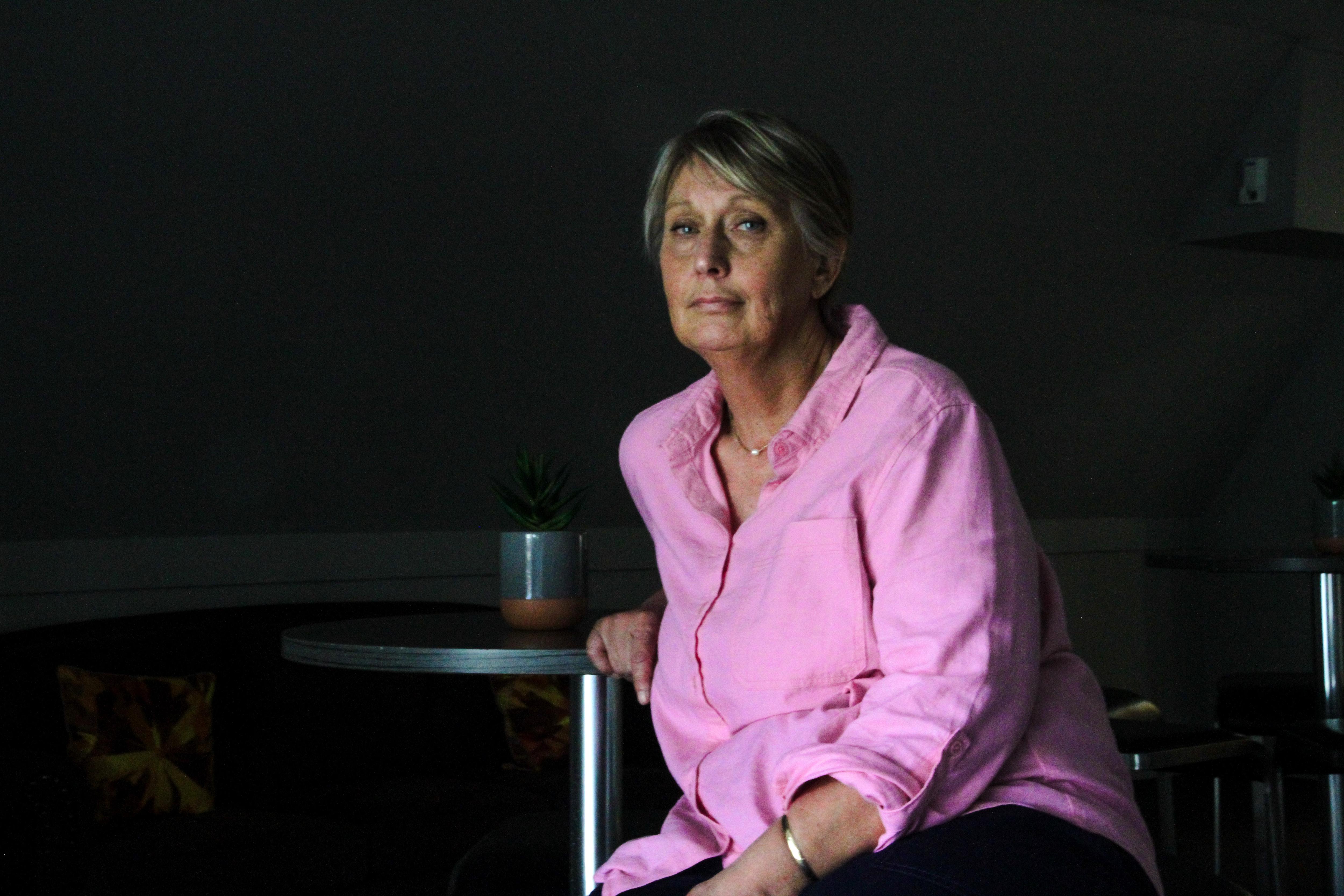 Woman in pink shirt sits down looking at camera