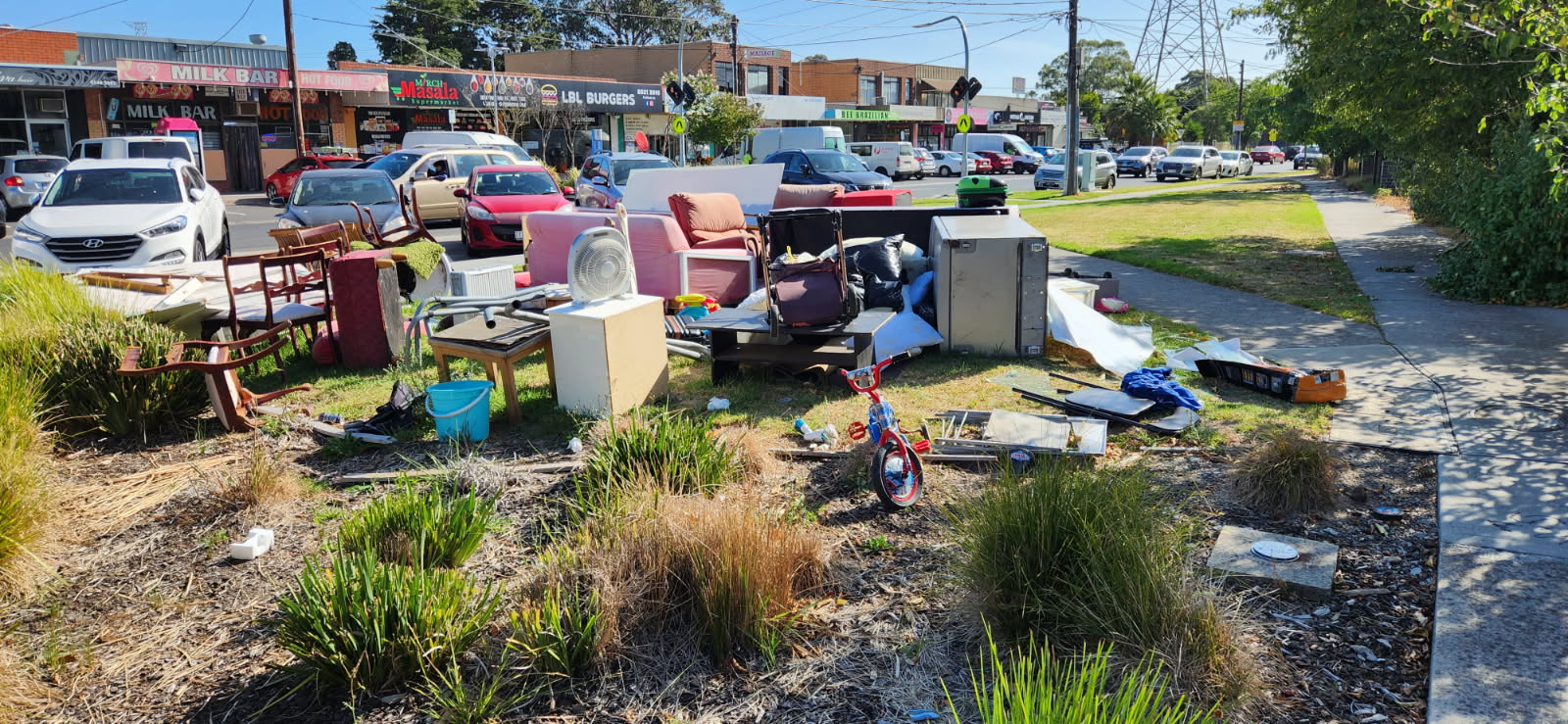 A large pile of household waste, on the side of a footpath and road, in a suburban street. 