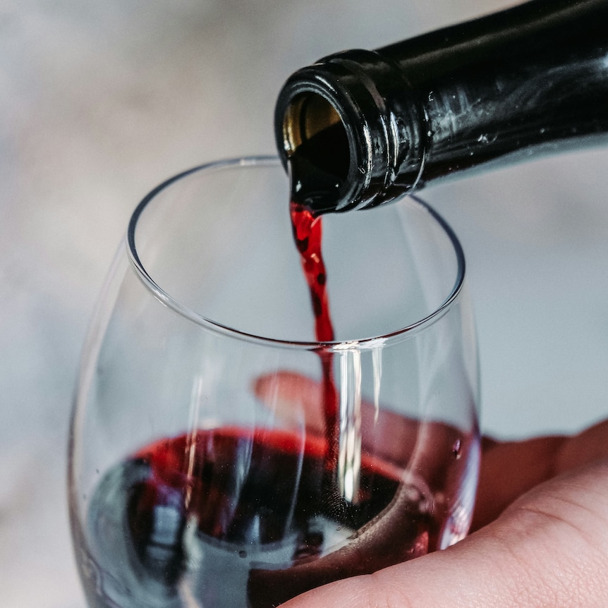 A bottle is tipped above a glass pouring red wine into it. 