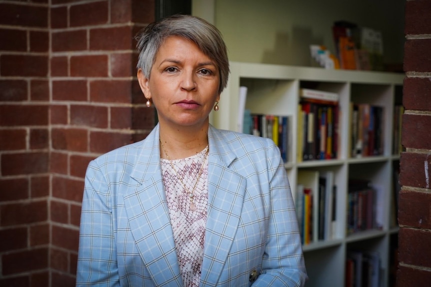 Hannah McGlade wears a blue blazer while standing in front of a bookcase