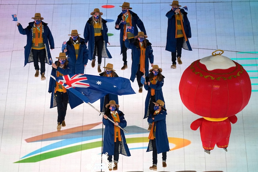 Melissa Perrine waves the Australian flag, she is surrounded by her teammates as they march together.
