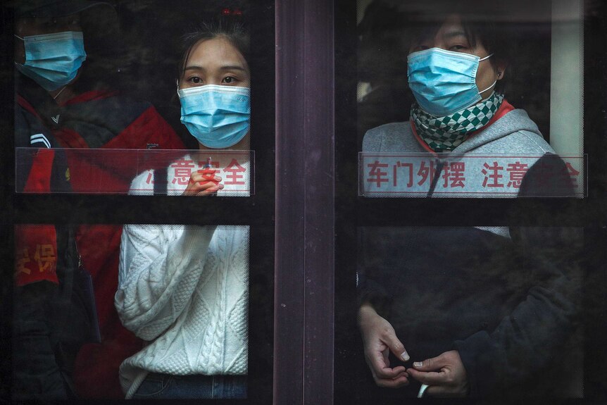 Commuters wearing face masks to help curb the spread of the coronavirus look out from a bus in Beijing.