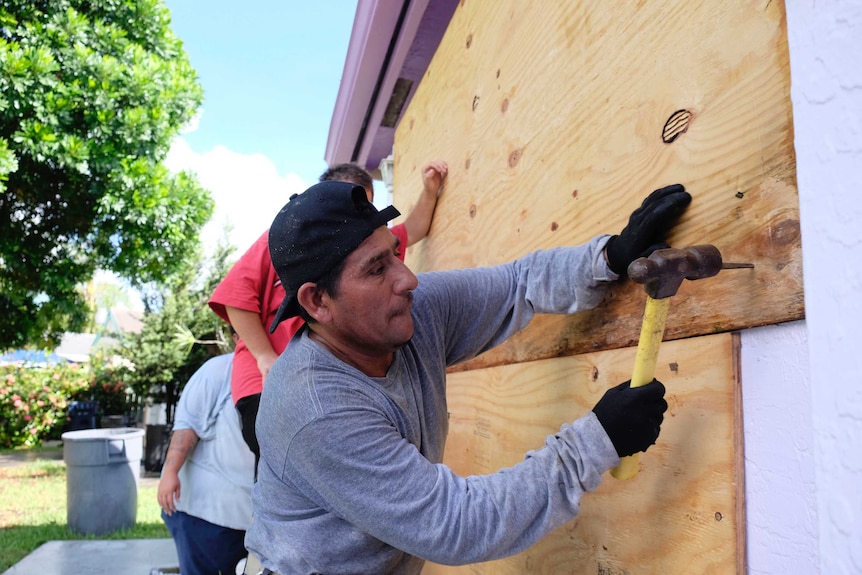 Men nail boards over the front of a house in Florida City.