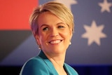 Standing at a podium smiling, Tanya Plibersek looks back over her should. Labor branding hangs above her.