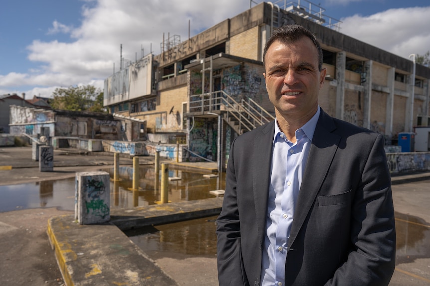 A man in a suit standing in front of an abandoned building with graffiti. 