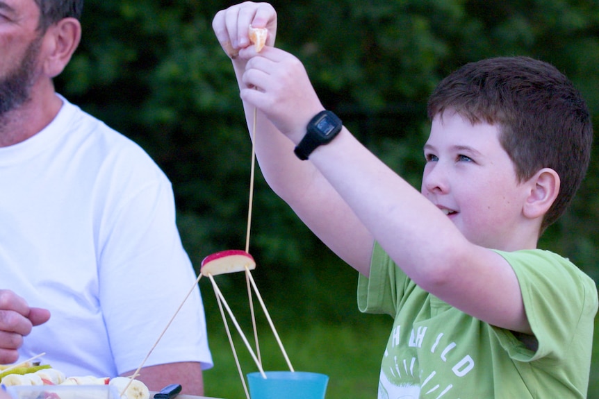 A little boy plays with skewers, apple and mandarin