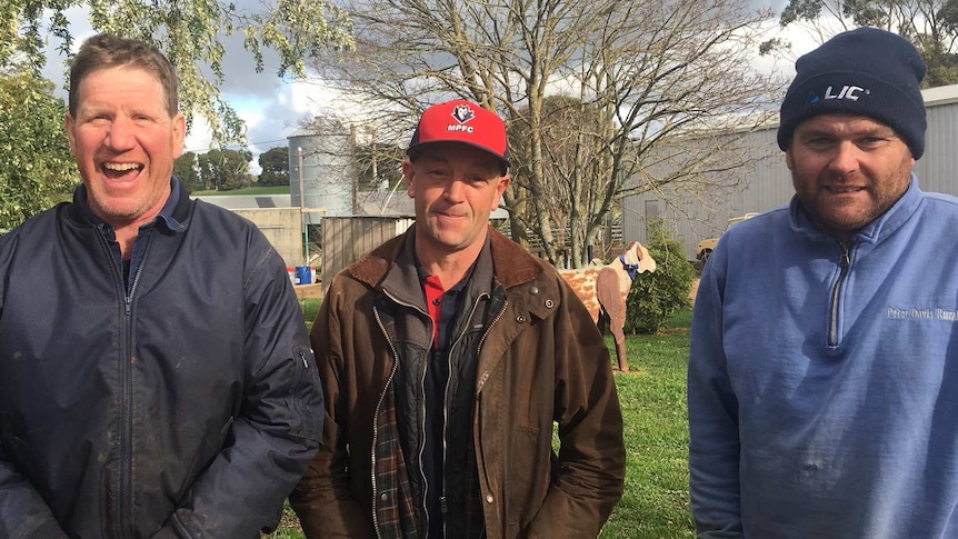 Three men stand in a yard all looking happy