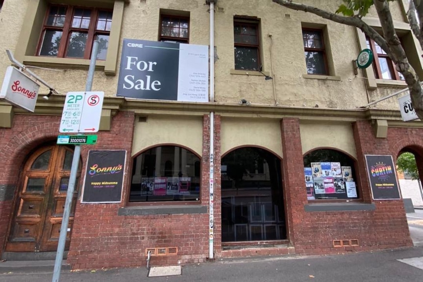 A red brick pub with a For Sale sign on it.