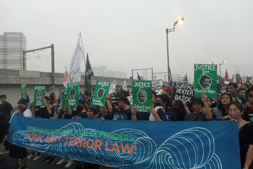 Protesters behind a blue banner that says ‘defend environmental defenders! junk anti-terror law!'