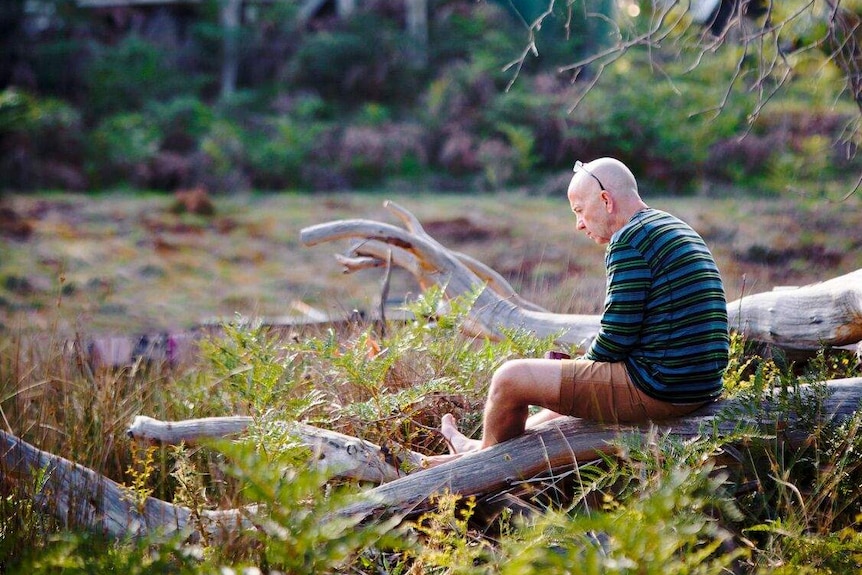 A man sits on a log at a Men's Gathrering