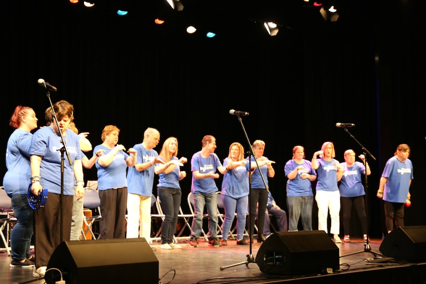 Group of about 12 adults standing on stage singing and doing sign language.