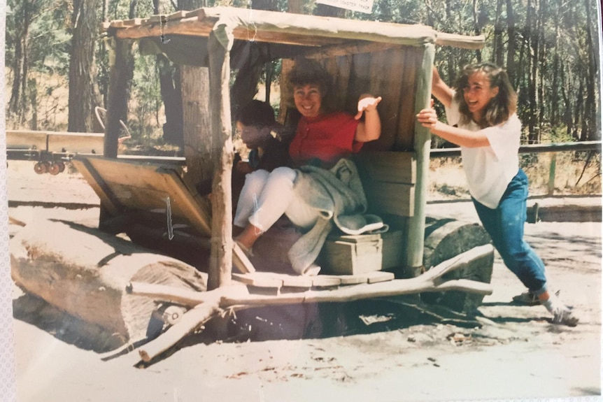 Two children and a woman pose for a photo in a pretend old car.