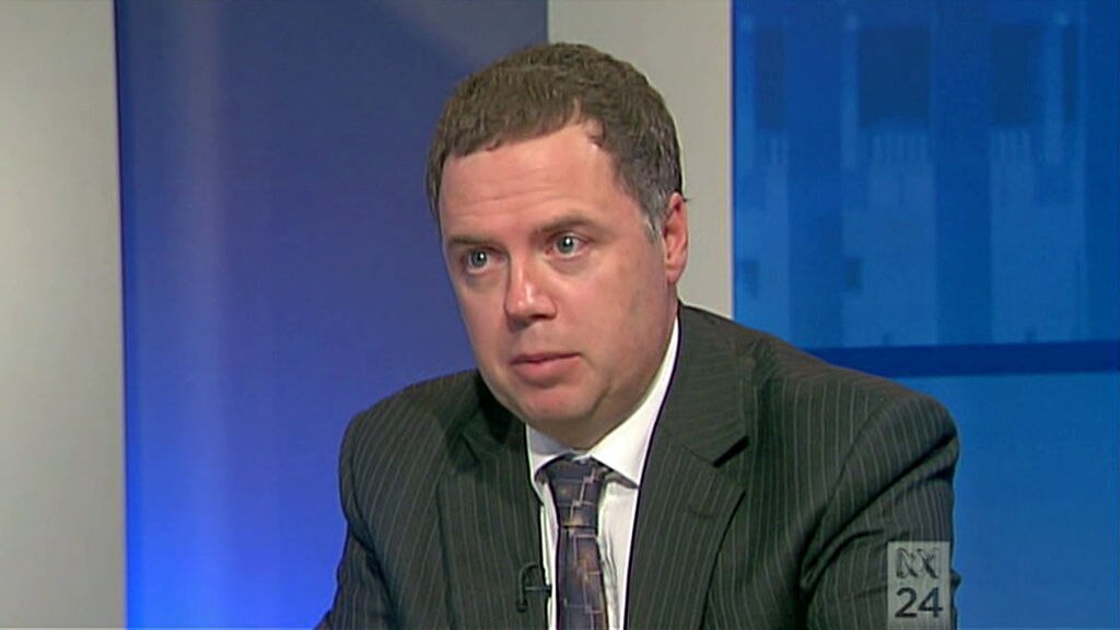 A man wearing a suit is interviewed in a television studio.