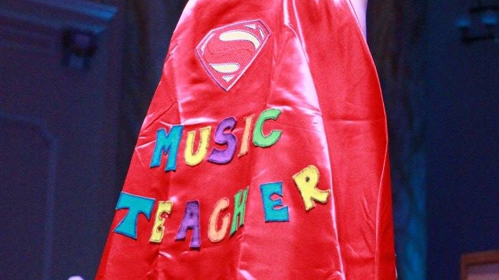A woman wearing a cape reading "Music Teacher" with a "superman" logo.