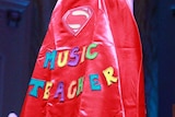 A woman wearing a cape reading "Music Teacher" with a "superman" logo.
