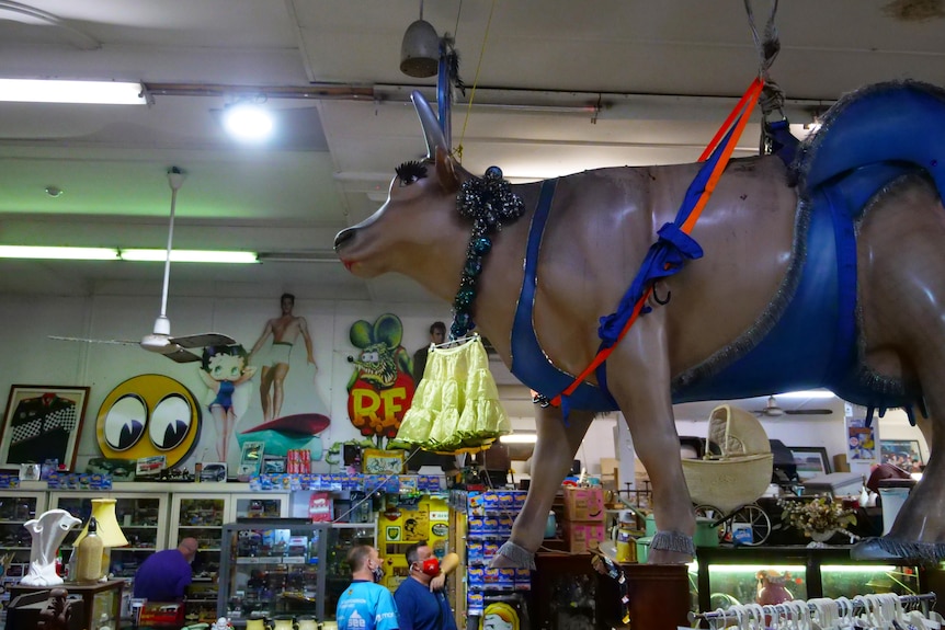 A statue of a cow wearing evening wear in a strange shop full of arcane material.