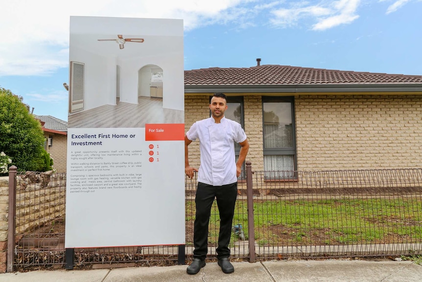 Ross stands in front of a house with a sign saying "excellent first home or investment".