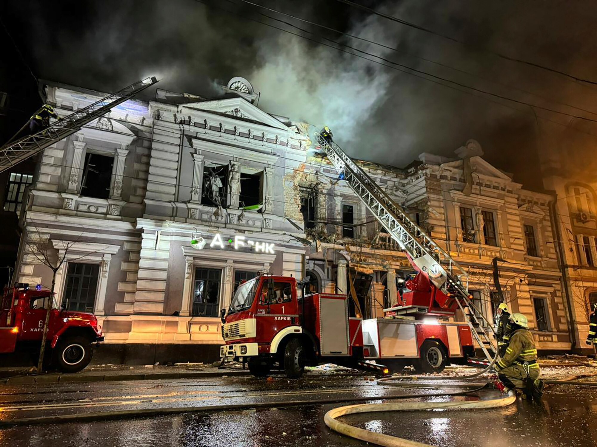 An old building with damage to it. A fire truck is outside with a crane over the building.