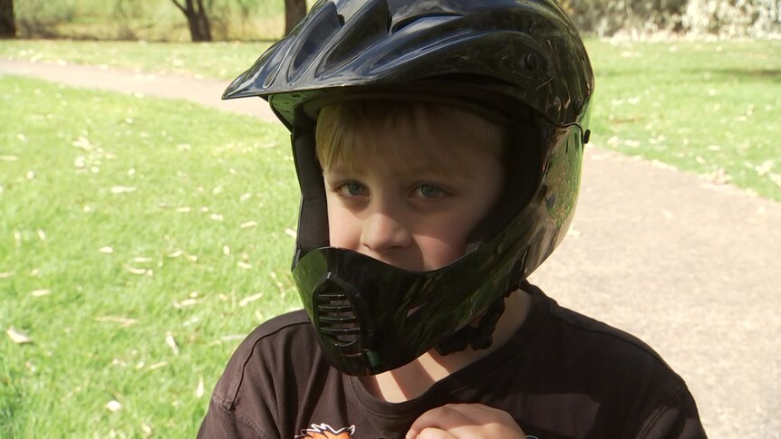A young boy with a black helmet and a path between two grassed areas behind him