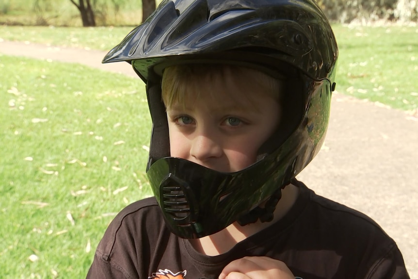 A young boy with a black helmet and a path between two grassed areas behind him