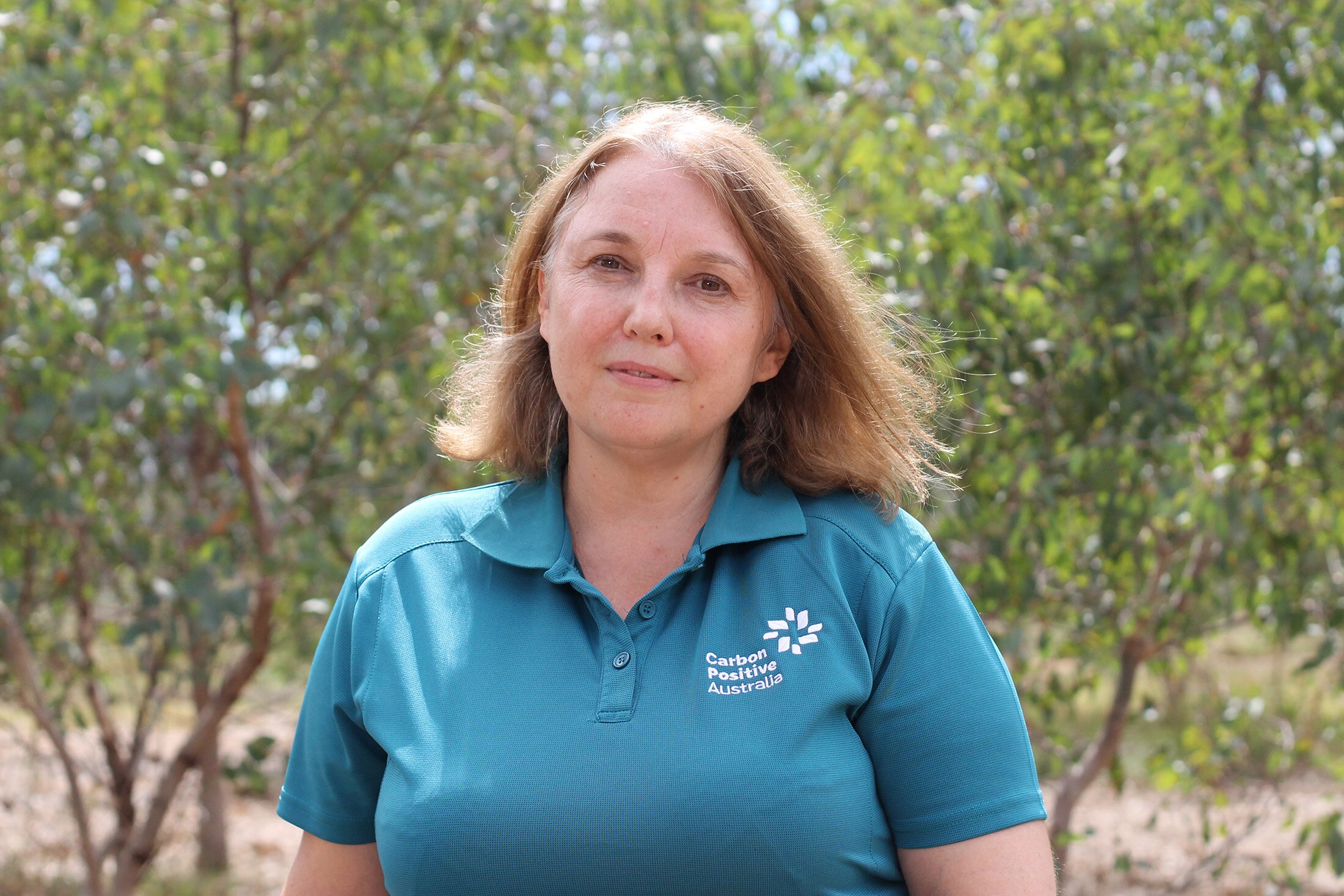 A mid-shot of a smiling woman wearing a turquoise polo shirt.