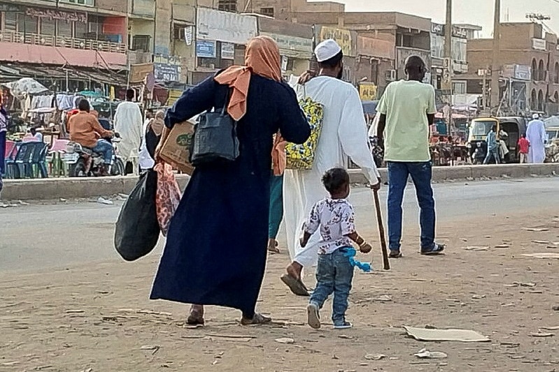 A woman walks with a small boy on a crowded dirt road. 