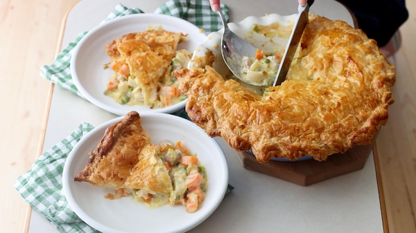 A home-cooked chicken pie being served onto two plates with a knife and serving spoon