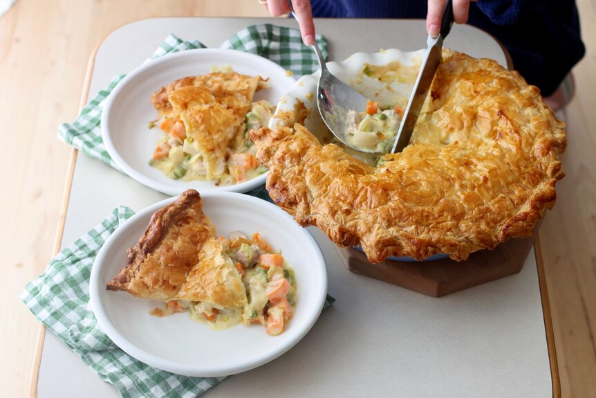 A home-cooked chicken pie being served onto two plates with a knife and serving spoon