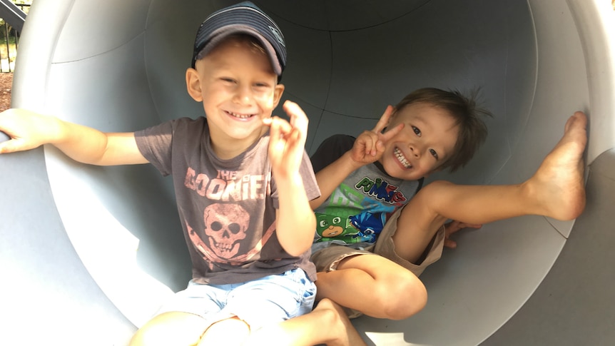 Two boys smile at the camera while sitting in the tunnel of a slide at a playgroup.