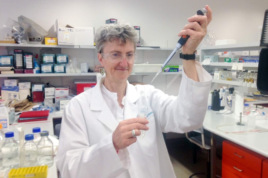 A woman, holding a syringe, looks at the camera