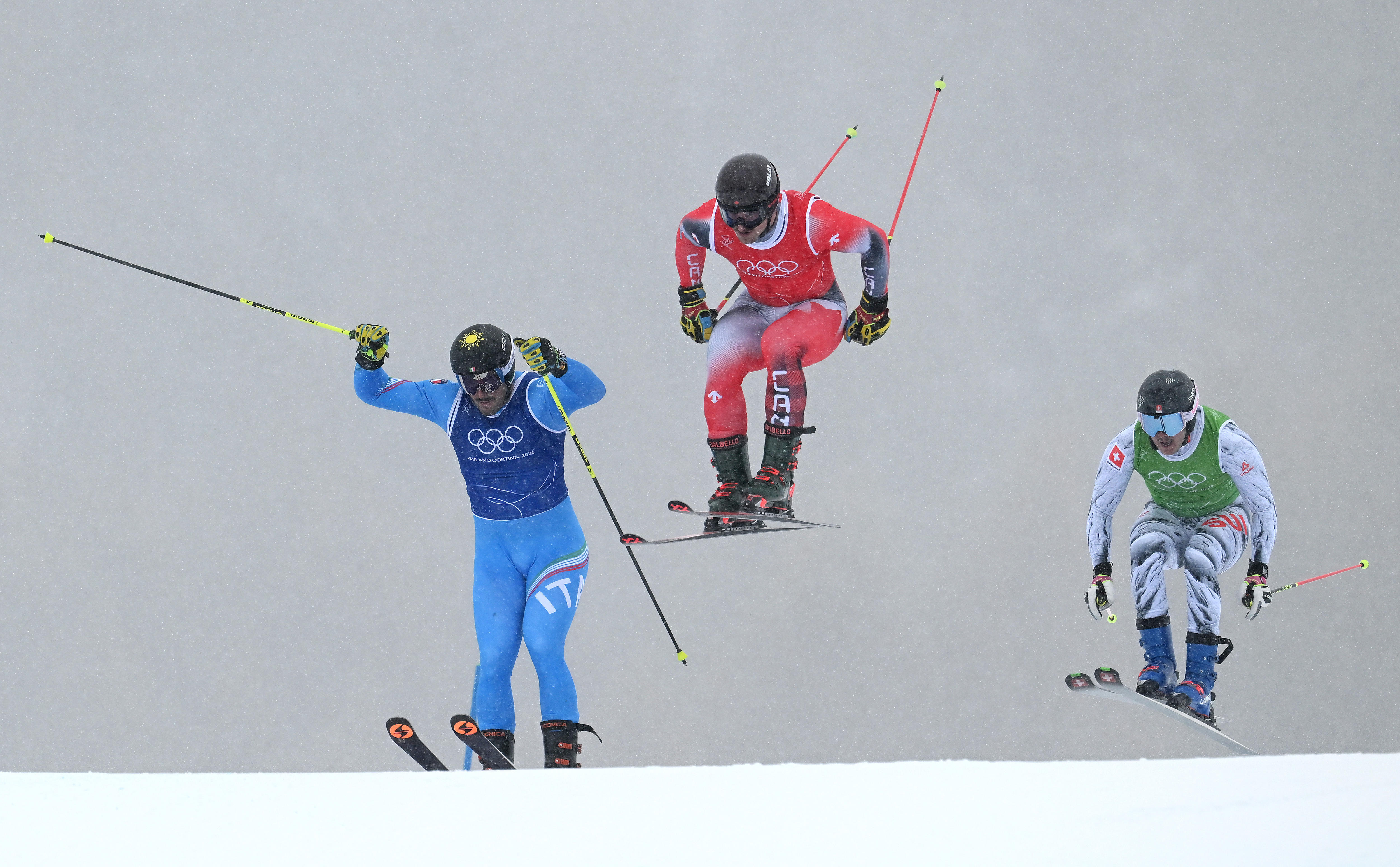 Three skiers jump in heavy snow.