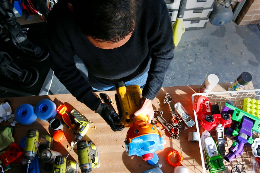 Bird's eye view of a man creating a colourful mini robot in his garage.