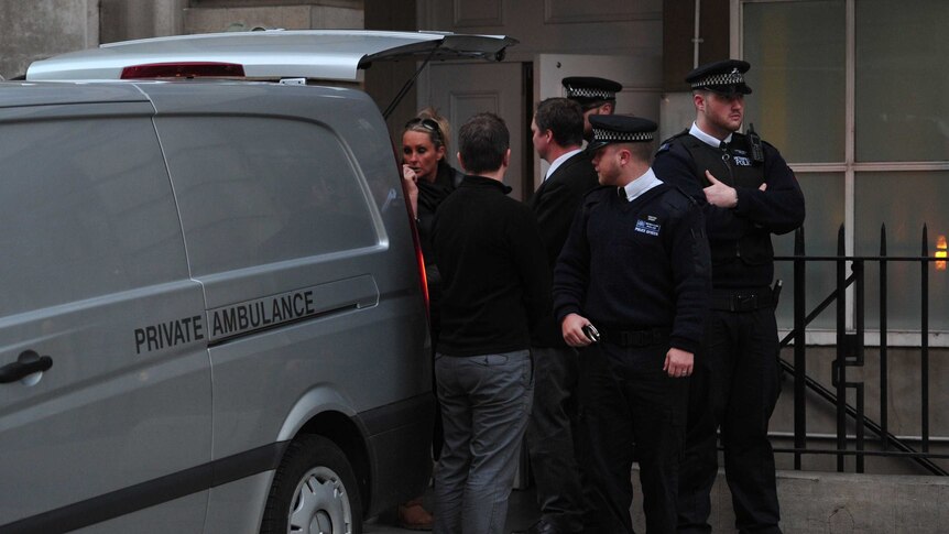 Police officers and hospital staff stand by the rear of a coroner's van