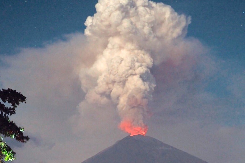 A woman stands in front of the erupting Mt Agung volcano in Bali