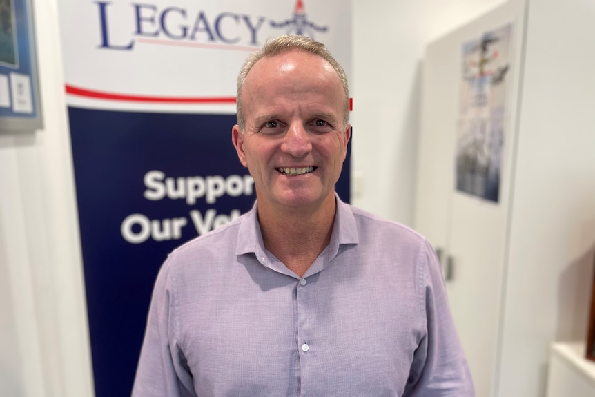 A man smiles for a photo in front of a Legacy banner.