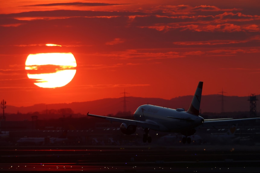 A passenger plane taxis along runway with beautiful orange sunset behind.