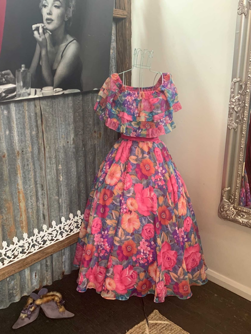 Colourful dress displayed on wire mannequin in dressing room with velvet curtains and giant mirror