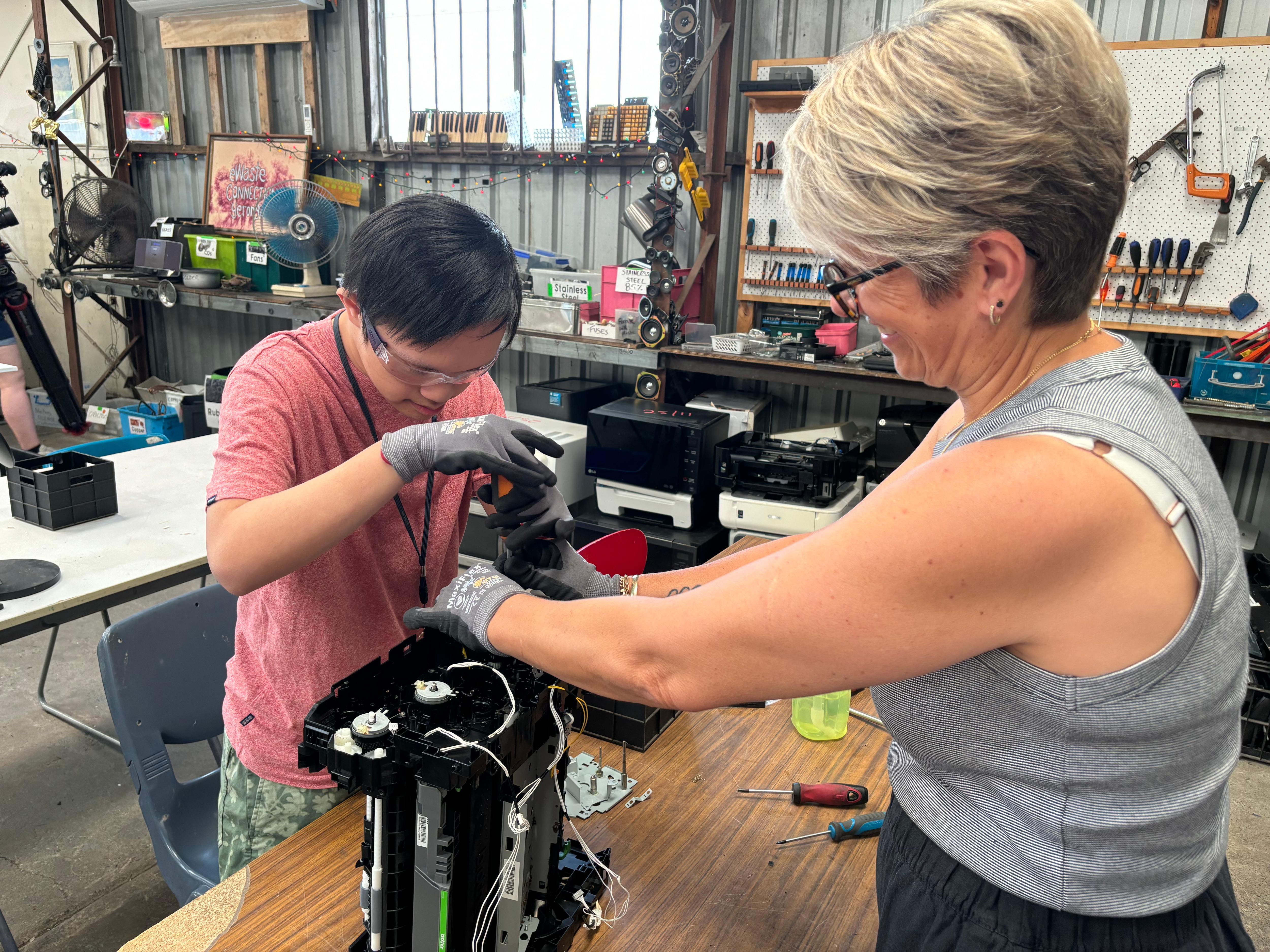 Un joven con gafas y una mujer usando herramientas para desmantelar desechos electrónicos