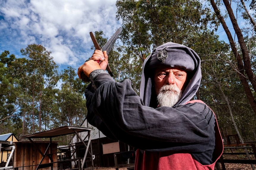 A man stands holding a sword above his head in a medieval village.