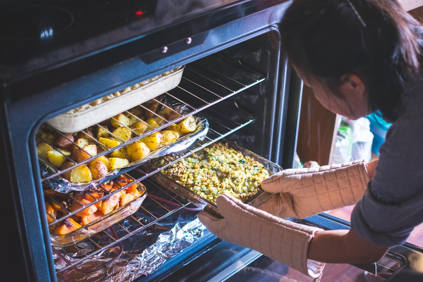 Woman putting trays of vegetables into oven