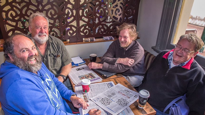 Four men sitting around a table at a coffee shop with papers open at the cross word
