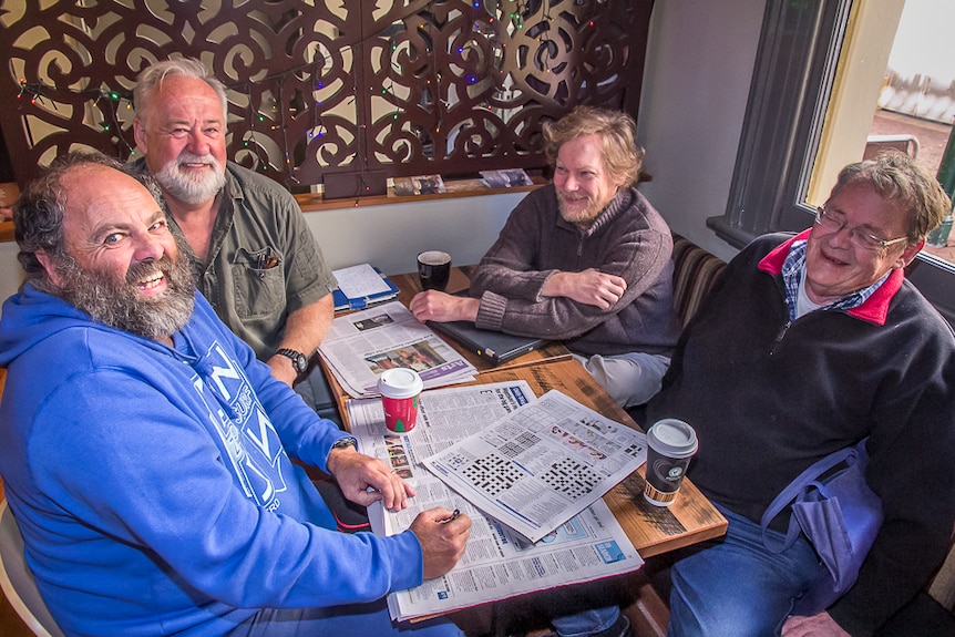 Four men sitting around a table at a coffee shop with papers open at the cross word