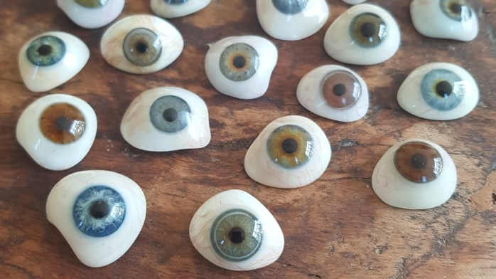 22 fake eyeballs with different coloured irises on a timber tabletop.