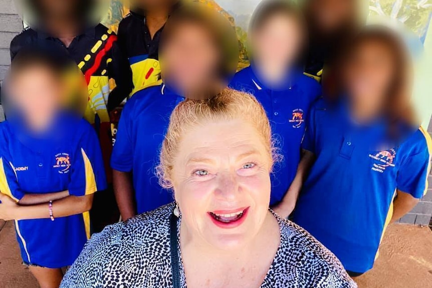 A woman surrounded by schoolchildren with blurred faces.
