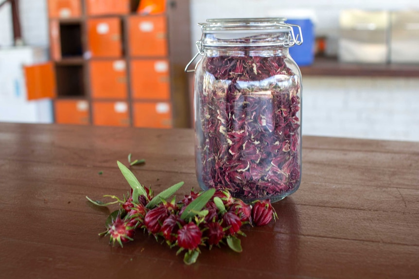 a jar of dried rosella and some rosella buds on a table.