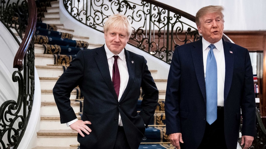 Boris Johnson stands with hands on his hips as Trump speaks next to him on a staircase.