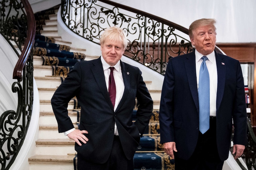 Boris Johnson stands with hands on his hips as Trump speaks next to him on a staircase.