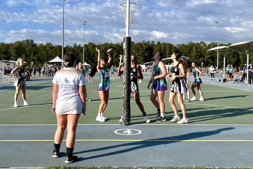 A netball umpire watching over players shooting a goal.