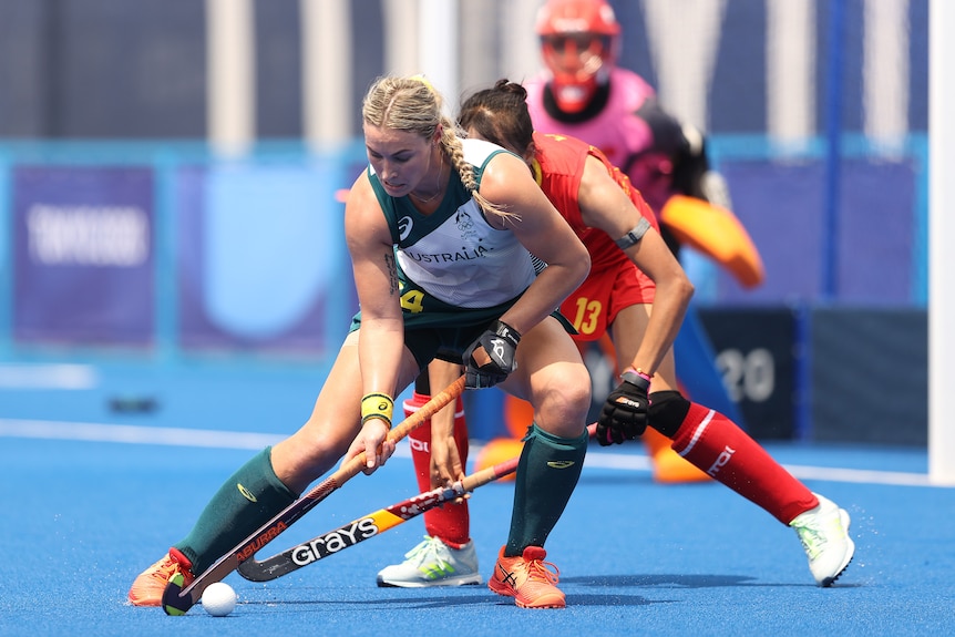 A blonde woman holding a hockey stick with a white ball in front of her